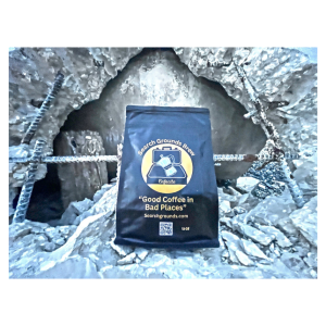 “Search Grounds Brew coffee bag in a rubble pile, showcasing the brand’s theme of providing good coffee in challenging environments.”