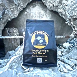 “Search Grounds Brew coffee bag in a rubble pile, showcasing the brand’s theme of providing good coffee in challenging environments.”